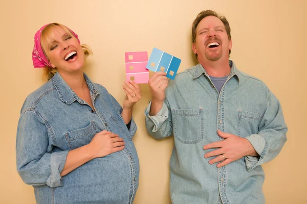 Grávida rindo casal decidir sobre rosa de pintura de parede azul — Fotografia de Stock