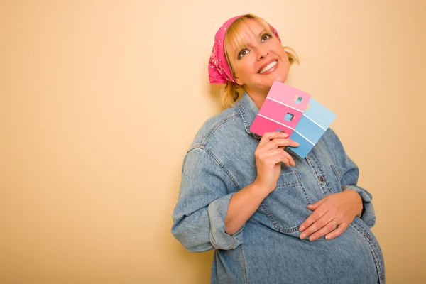 ピンクとブルー塗装見本を保持壁にもたれかかって物思いにふけるの妊娠中の女性の笑みを浮かべてください — ストック写真