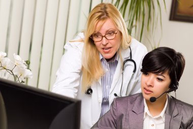 Female Doctor Discusses Work on Computer with Receptionist Assis clipart