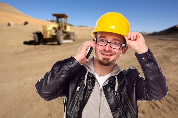 Молодой строитель на сотовом телефоне в грязном поле с трактором — стоковое фото