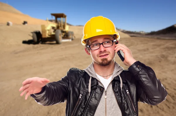 Jonge cunstruction werknemer op mobiele telefoon in vuil veld met tract — Stockfoto