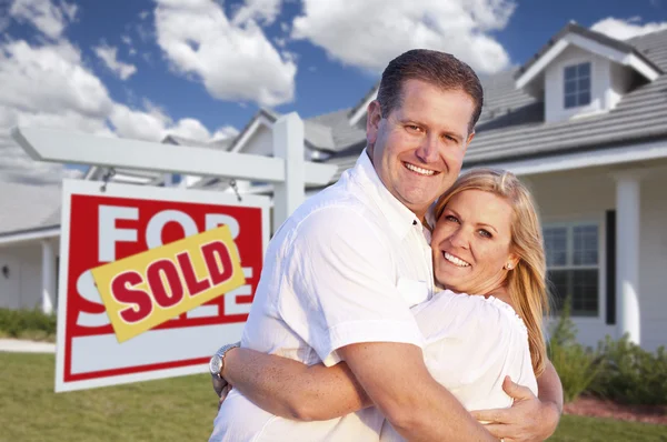 Casal abraçando na frente do sinal de venda e casa — Fotografia de Stock