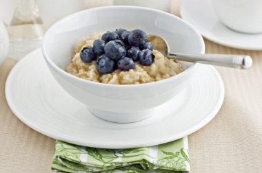 Large flake whole oatmeal with blueberries and brown sugar on white china makes a healthy breakfast clipart