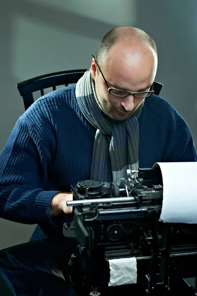 Старомодный лысый писатель в очках пишет книгу на винтажной пишущей машинке Лицензионные Стоковые Изображения