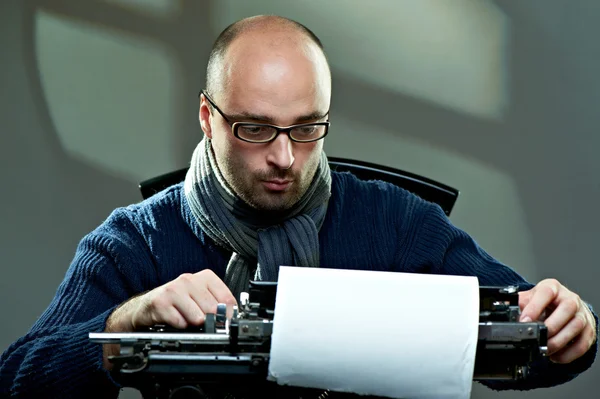 Старомодный лысый писатель в очках пишет книгу на винтажной пишущей машинке — стоковое фото