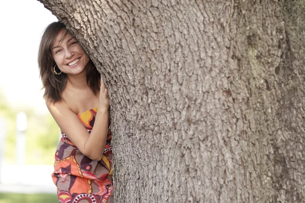 Mulher sorrindo atrás da árvore — Fotografia de Stock