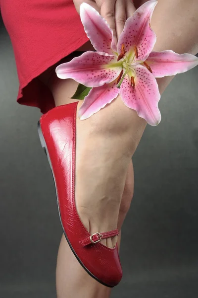 Vacker kvinna benen röda klackar och blomma — Stockfoto