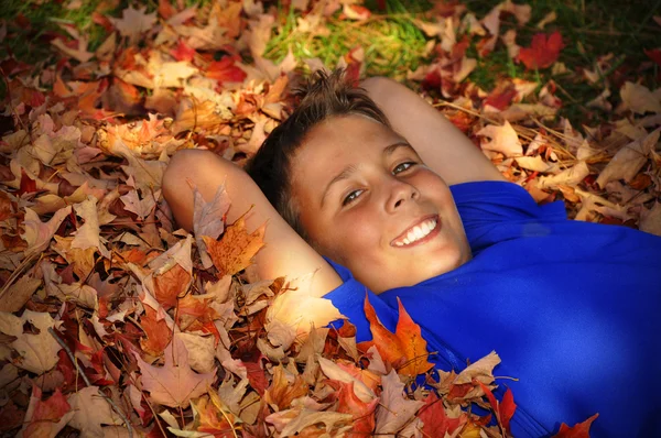 Preteen menino que estabelece em folhas de outono — Fotografia de Stock