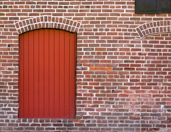 Стена из красного кирпича с красной дверью и окном — стоковое фото
