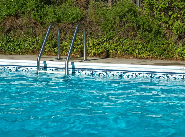Acqua blu della piscina. Scala e bordo piscina in piena luce del sole — Foto Stock