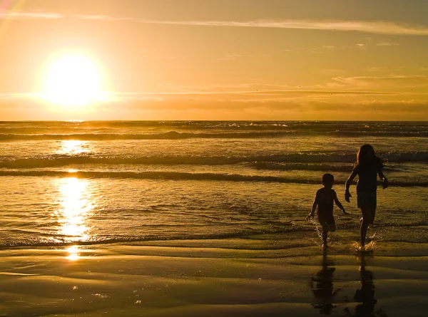 Silhuetas de crianças brincando na praia contra o pôr do sol — Fotografia de Stock