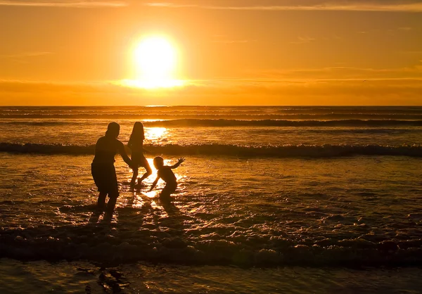 stock image Silhouettes of children playing on the beach against the sunset