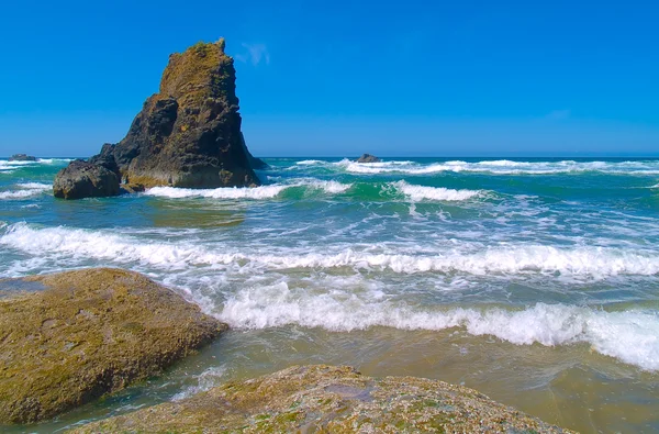 Stenig strand med vågorna kraschar på sand — Stockfoto