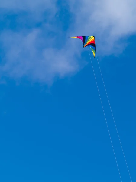 Um arco-íris colorido stunt pipa contra um céu azul com nuvens wispy . — Fotografia de Stock