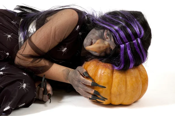Menina vestida como uma bruxa apoiada em uma abóbora Imagens De Bancos De Imagens