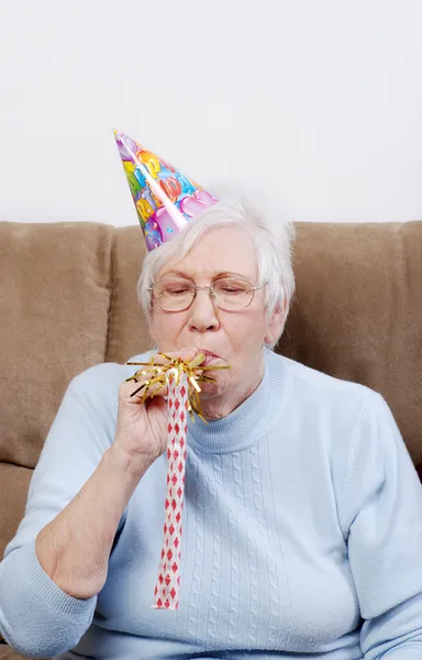 Mujer mayor con sombrero de cumpleaños soplando un fabricante de ruido —  Fotos de Stock