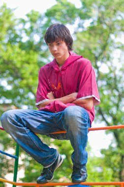 The teenager sitting on a swing in park and thinking clipart