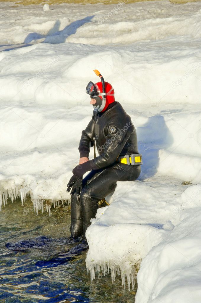 Diver in water on white ice at winter