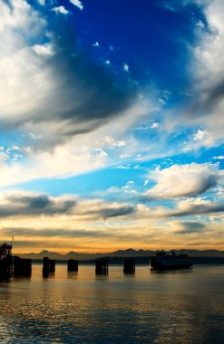 A beautiful scenery of a ferry coming into a dock against the Olympic Mountains during the sunset clipart