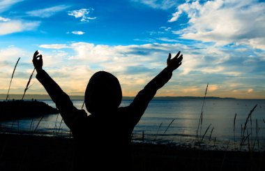 A praying woman in silhouette during the sunset clipart