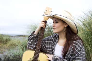 A beautiful girl posing with a guitar at the beach clipart