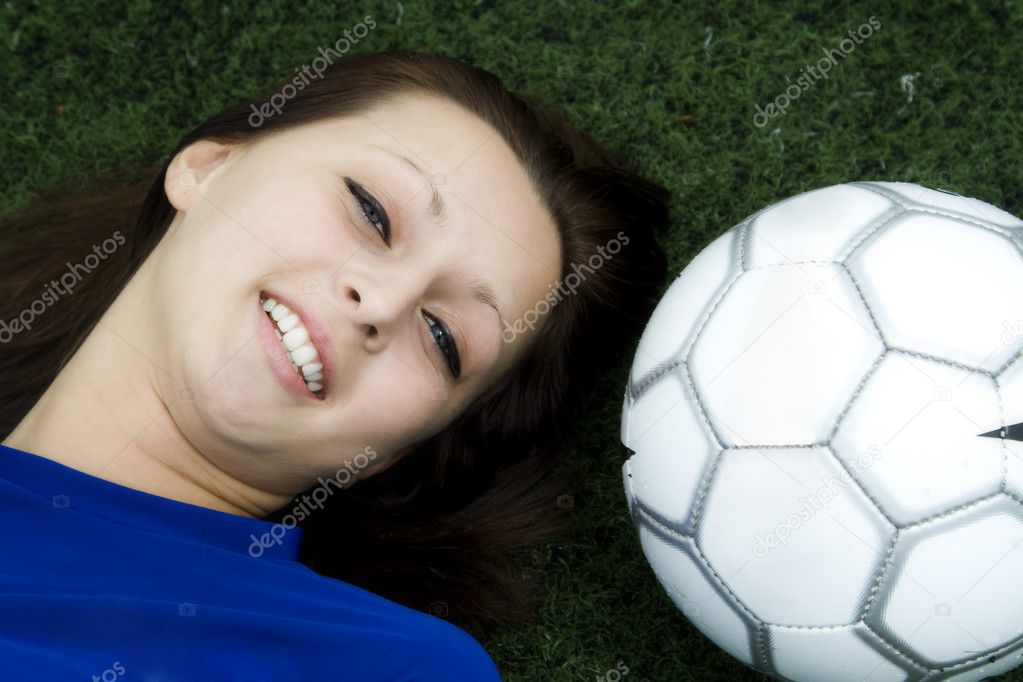 A beautiful young girl lying down on the grass next to a soccer ball