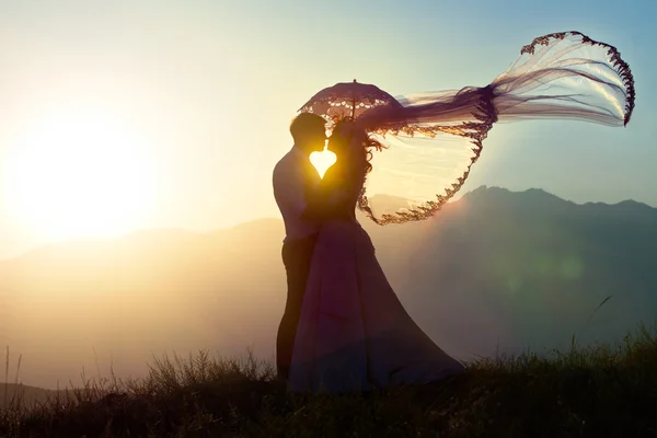 Brudgummen och bruden kiss i bergen mot en nedgång. — Stockfoto