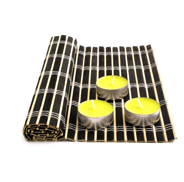 白い背景の上の つの小さい黄色の蝋燭と黒竹マット — ストック写真