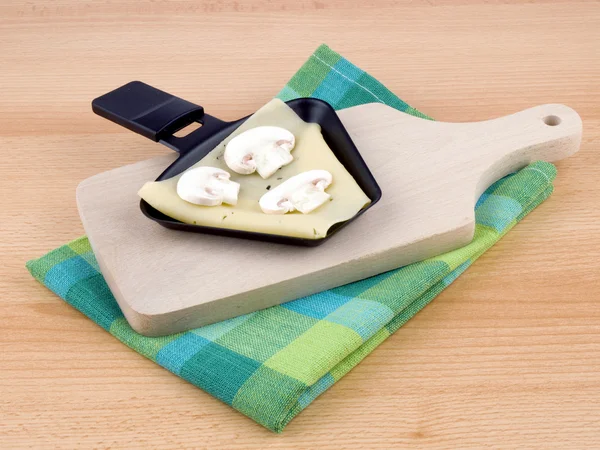 Raclettepfanne mit Käse und Champignons - Party-Essen Stockfoto
