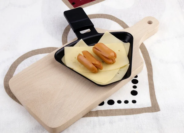 Raclette pan with cheese and sausages - party food — Stock Photo, Image