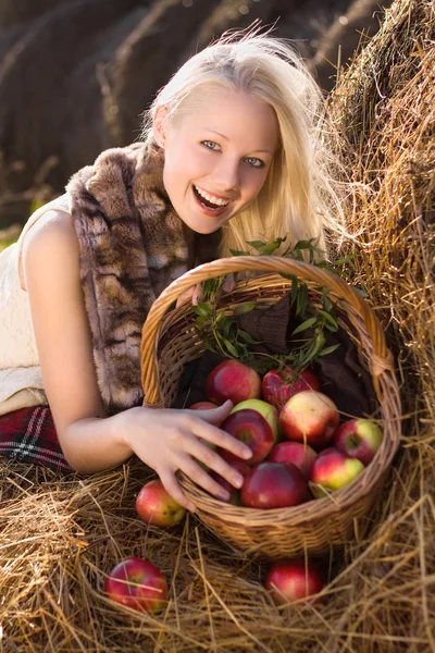 Linda loira sorridente com muitos maçã no cesto na hays — Fotografia de Stock