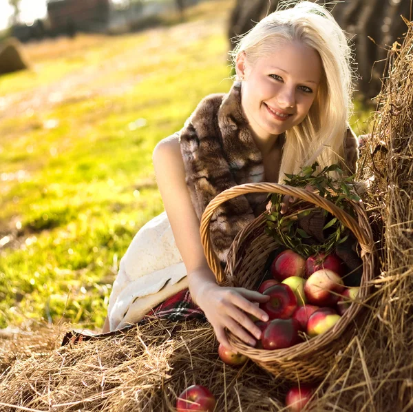 漂亮的金发微笑着女人和许多苹果在农场的干草堆上篮 — 图库照片