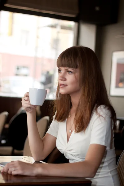Hétköznapi fiatal nő kávézóban kávét kortyolgatva — Stock Fotó