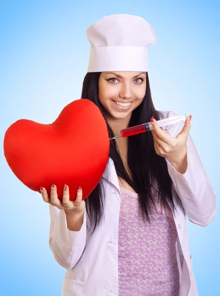 Gelukkig vrouwelijke arts injecteren een injectiespuit in het rood hart op blauw — Stockfoto