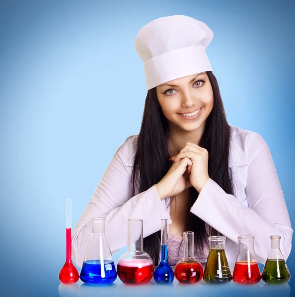 Jonge wetenschapper aan de tafel met reageerbuisjes op blauwe achtergrond — Stockfoto