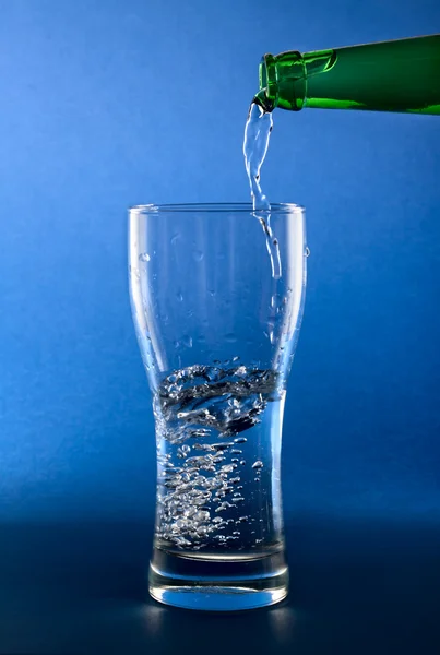 Versando acqua pulita in vetro su sfondo blu — Foto Stock