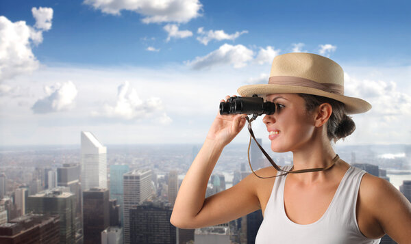 Smiling woman using binoculars with cityscape on the background