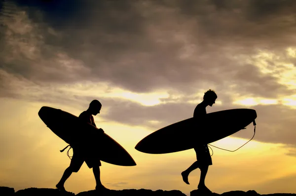 Dos surfistas llevando sus tablas a casa al atardecer Imagen de stock