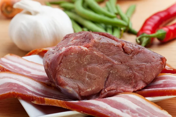 Carne crua e listras de bacon em uma mesa de madeira — Fotografia de Stock