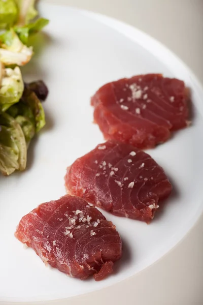 Три ломтика сырого тунца с солью и салатом — стоковое фото