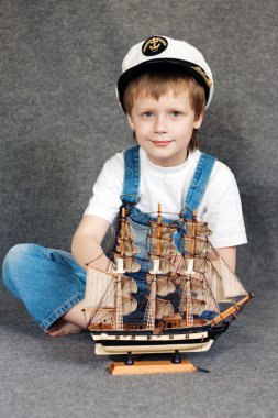 Portrait of the cute dreaming child with the model ship. clipart