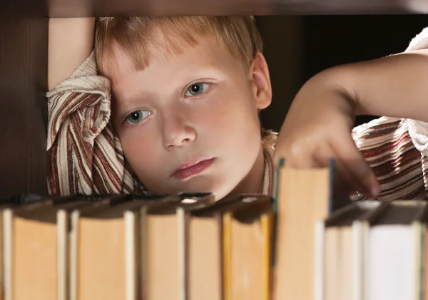The boy at a bookcase gets the book. — Stock Photo, Image