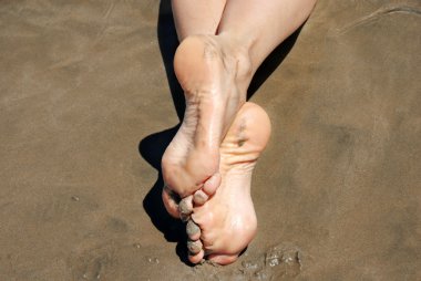 Female crossed feat in sand on beach clipart