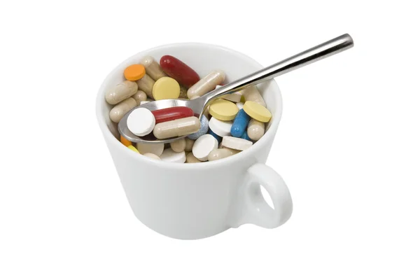 Cup of multicolored tablets and capsules with spoon — Stock Photo, Image