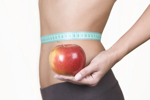 Frau hält einen roten Apfel, während sie ihre Taille misst — Stockfoto