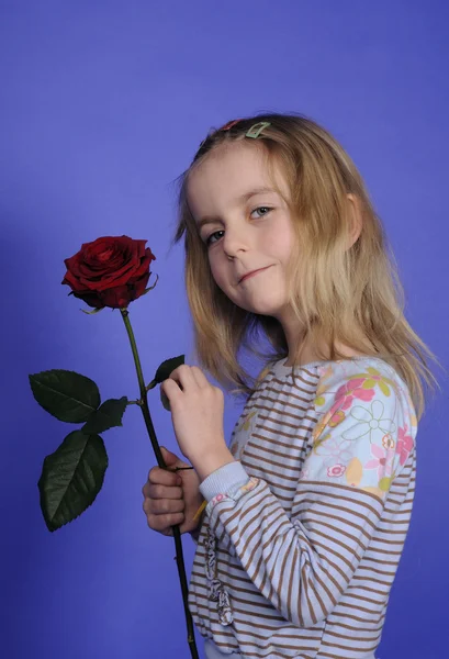红玫瑰在蓝色背景前的金发小女孩 — 图库照片
