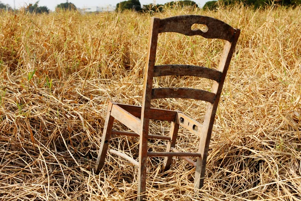 Cadeira de madeira quebrada no campo de grama seca — Fotografia de Stock