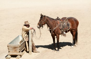 Cowboy with his horse at a water trough clipart