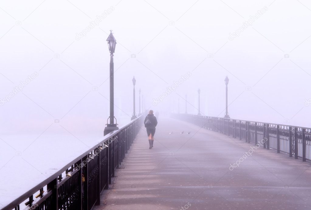 Landscape with lonely lady crossing a bridge in the misty morning