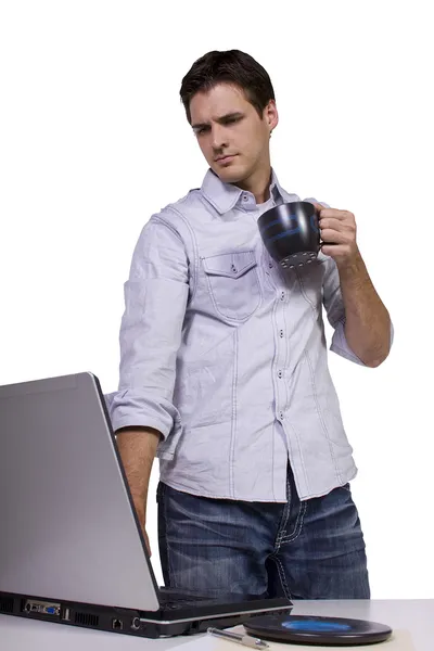 Молодой человек пьет кофе и работает на ноутбуке — стоковое фото